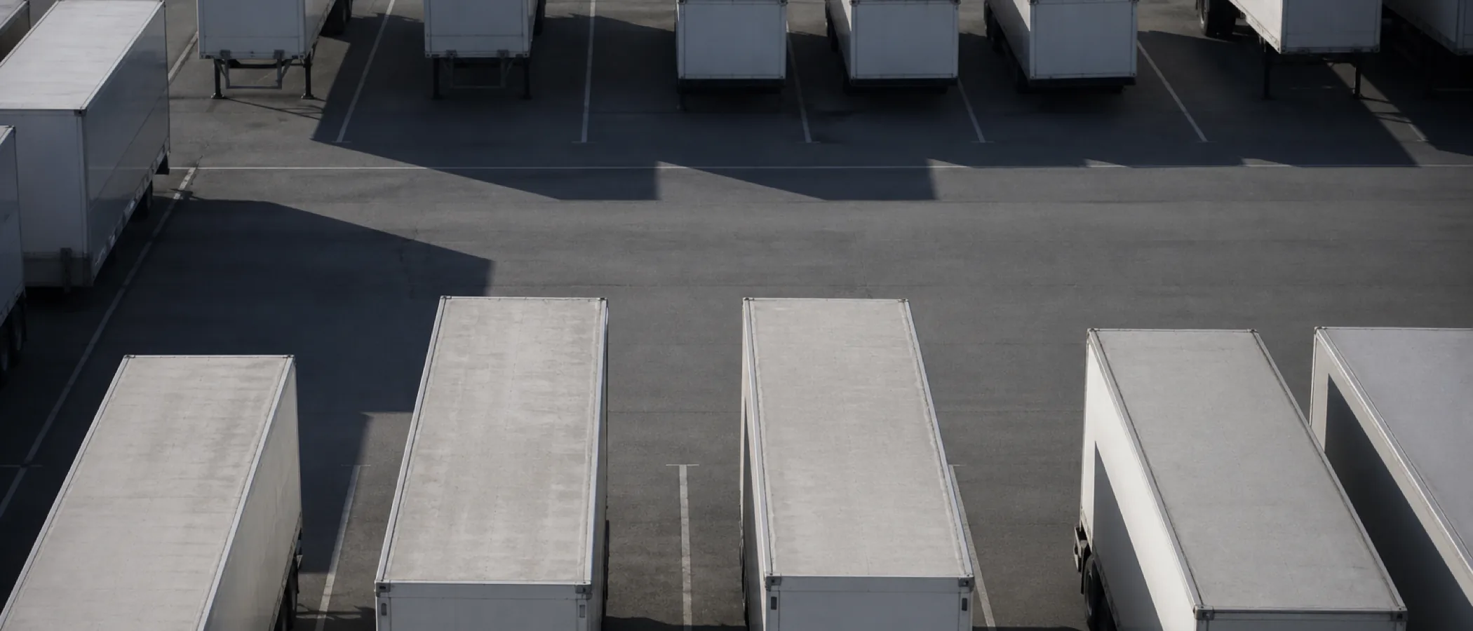 An elevated view down onto a trailer parking yard, rows of unmarked box trailers and swap bodies standing in painted bays across grey tarmac.
